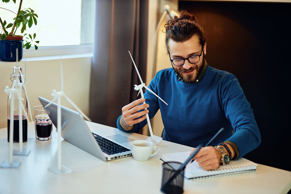 Attractive bearded environmentalist sitting in his office and drawing new windmill model.