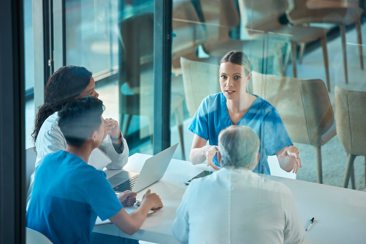 Medical team, doctors and meeting with a laptop for a discussion, planning or research at table. Men and women healthcare group talking about communication strategy, virus or surgery in a hospital.