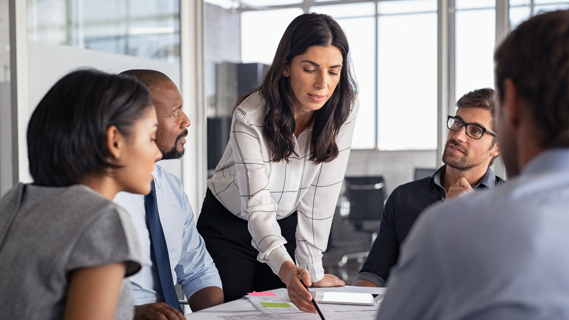 Team of multiethnic architects working on construction plans in meeting room. Engineers and designers discussing project in office. Businesswoman with business team in conference room working on blueprint.