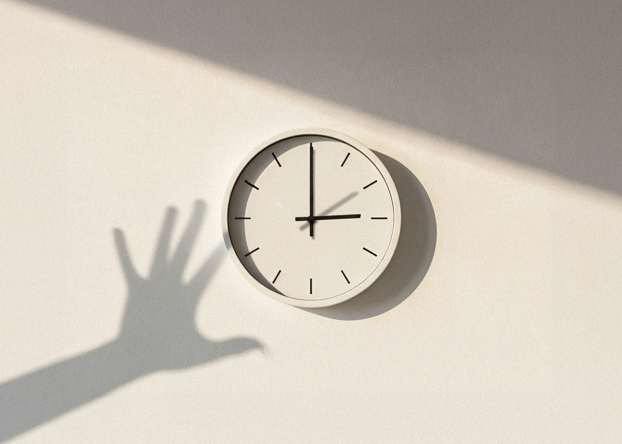 Eine analoge Wanduhr mit dem Schatten einer Hand,